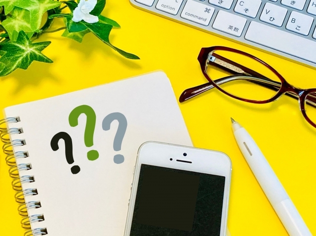 クエスチョンマークが書かれたノートとパソコンとメガネ