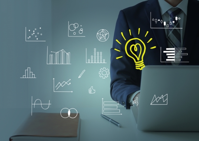 パソコンで仕事をする男性の横に浮かぶイラスト