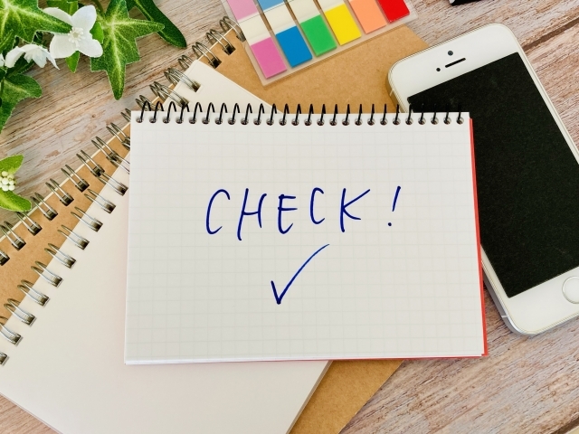 チェックの文字が書かれたノートとスマホ、付箋